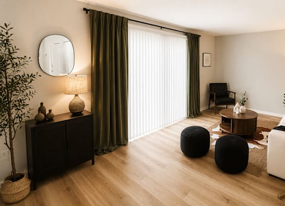 A living room with a white sofa, a wooden coffee table, and a large window with curtains.