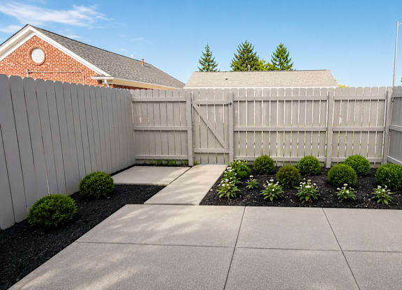 A backyard with a concrete patio and a white picket fence.