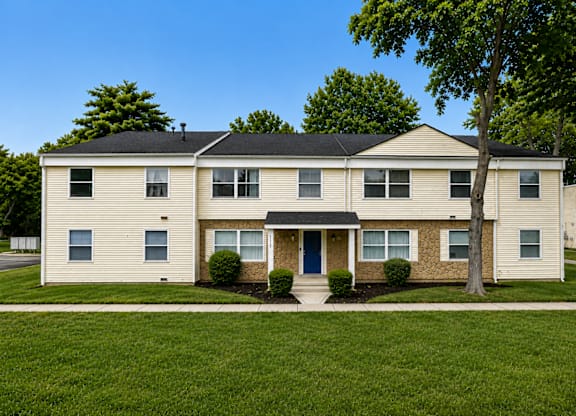 A beige house with a black roof and a tree in front.