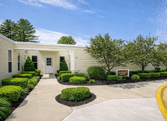 A building with a white door and windows surrounded by bushes and trees.