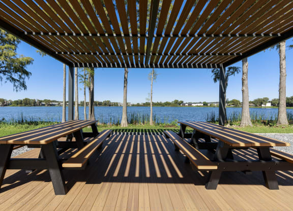 two picnic tables under a pergola overlooking a lake