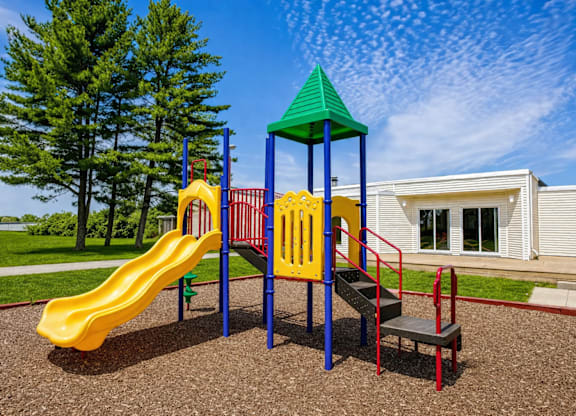A playground with a yellow slide, a green roofed structure, and a red ladder.