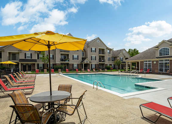 A pool area with chairs and umbrellas in front of apartment buildings.