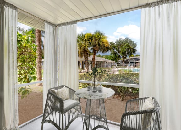 a patio with white curtains and a table and chairs at Aqua Bay Apartments in Naples, FL 34116