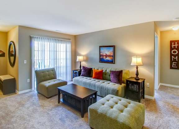 A living room with a couch, chair, ottoman, and lamp.