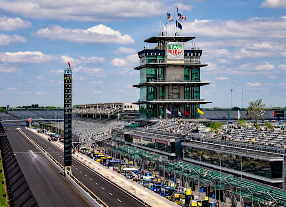 A view of a race track with a large building in the background and a crowd of people in the foreground.
