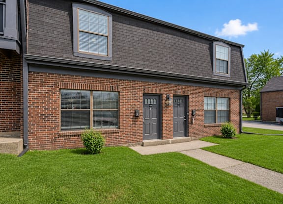 A brick house with a grey roof and a small green bush in front.