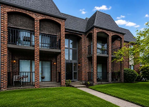 A red brick building with a balcony and a green lawn in front.