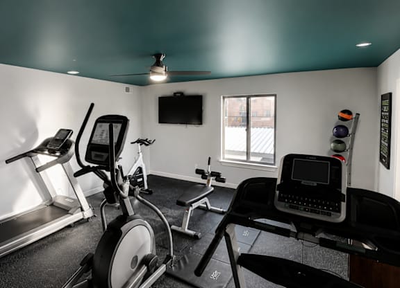 A room with a treadmill, exercise bike, and a television.