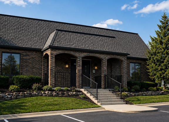 A small brick building with a black roof and a stone wall in front.