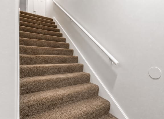 A staircase with a brown carpeted runner and white handrail.