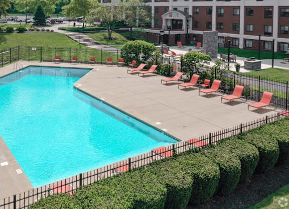 A large swimming pool surrounded by red lounge chairs and green bushes.