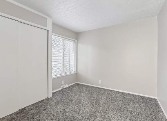 A room with a carpeted floor and a window with blinds.