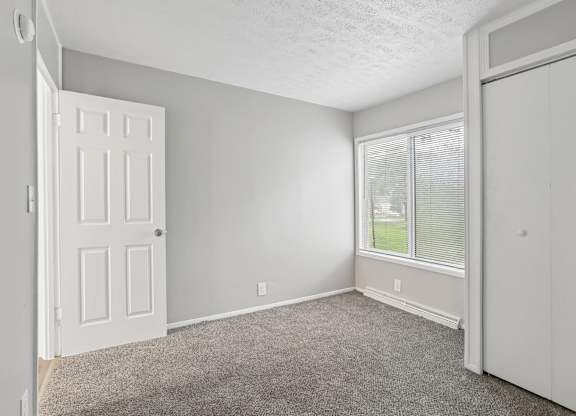 A room with a carpeted floor, a door, and a window with blinds.