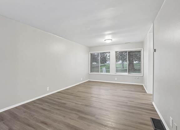 A room with wooden flooring and a window with a view of trees.