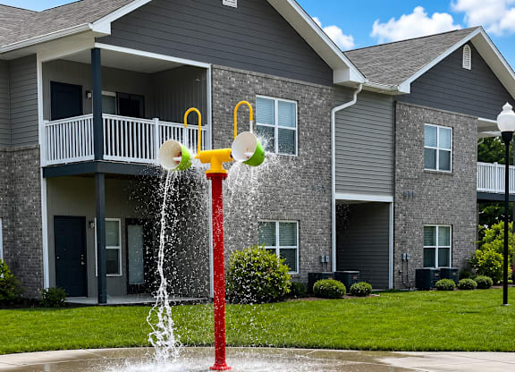 A water fountain with a yellow and red spout in front of a grey building.