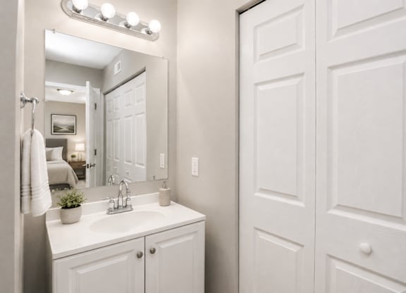 A white bathroom with a sink, mirror, and lighting fixture.