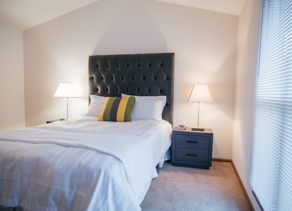 a bedroom with a bed and a nightstand with two lamps and a window
