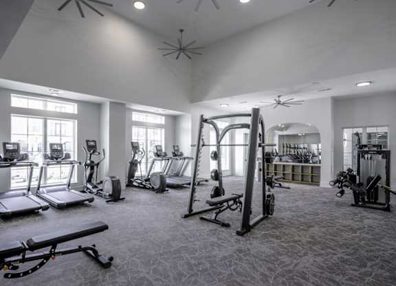 a gym with cardio equipment and weights in a building with windows