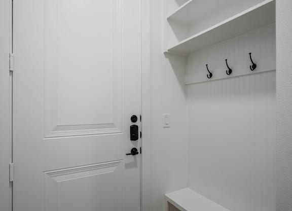 a white door with a black door knob and black hooks on the wall entryway
