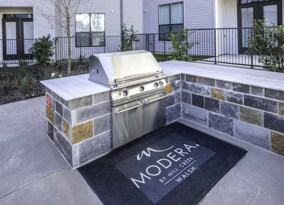 an outdoor kitchen with a grill and a rug in front of a building