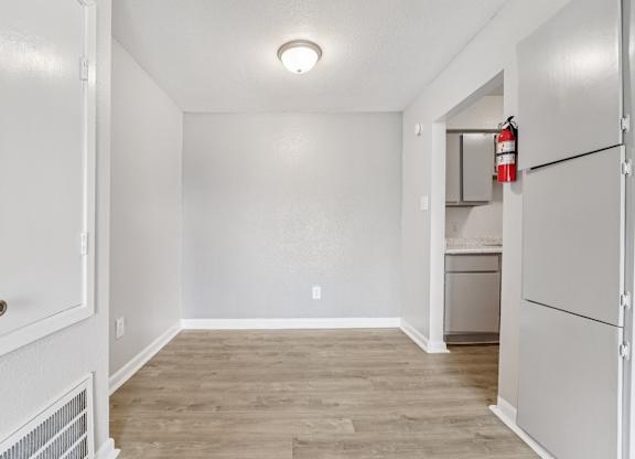 A white door opens to a room with a wood floor and a white wall.