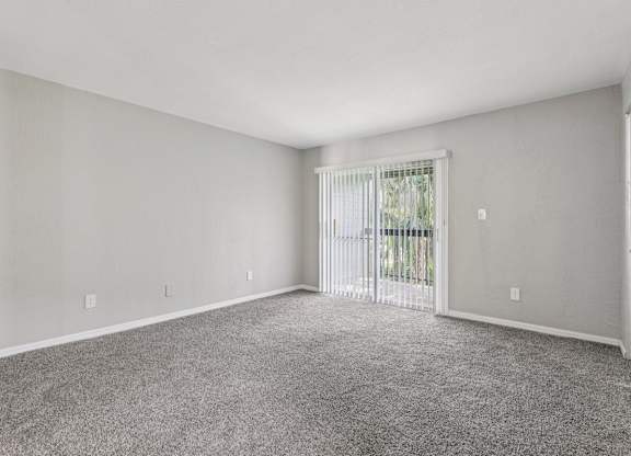 A spacious room with a carpeted floor and a sliding glass door leading to a balcony.