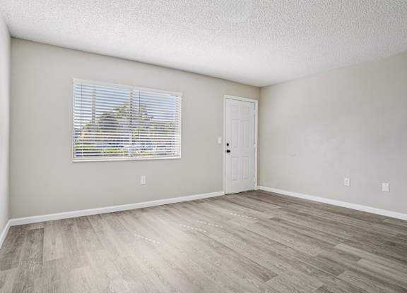 A room with a wooden floor and a window with blinds.