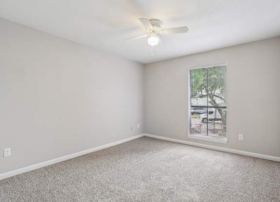 A room with a ceiling fan and a window showing a parking lot outside.