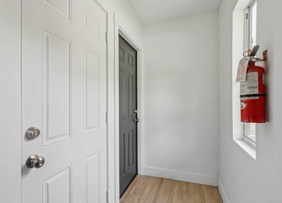 A white door with a silver handle is next to a red fire extinguisher.