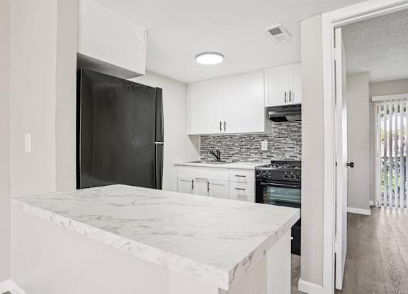 A kitchen with a marble countertop and a black refrigerator.