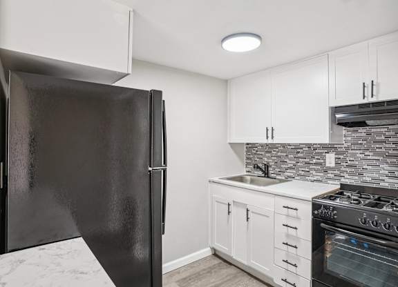 A black refrigerator stands in a kitchen with white cabinets and a marble floor.