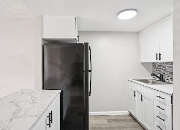 A black refrigerator stands in a kitchen with white cabinets and a marble countertop.