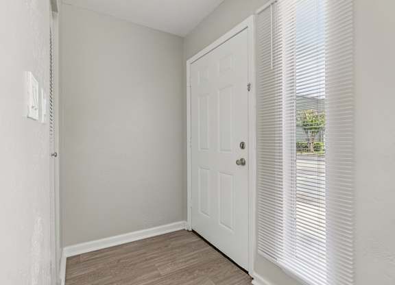 A white door is in a room with a window covered by blinds.