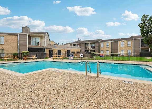 A swimming pool surrounded by a stone patio and apartment buildings.