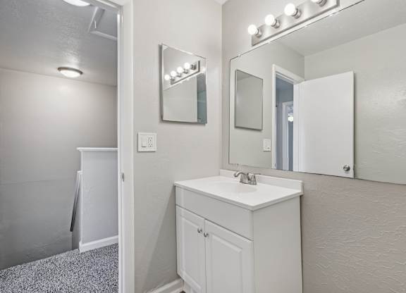 A white bathroom with a sink, mirror, and lighting.