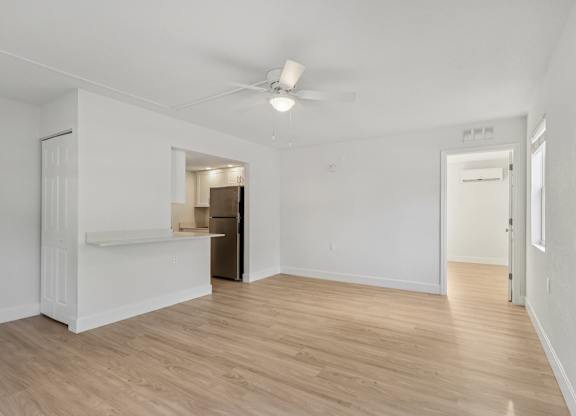 A room with a ceiling fan and light, wooden floors, and white walls.
