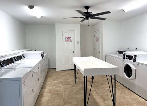 A laundry room with a table and washing machines and dryers.