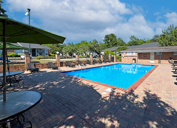 The large sundeck with loungers and picnic tables with umbrellas at the Pool at Ascot Place Apartments