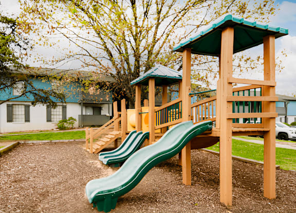 a playground with a wooden playset with plastic slides at Crestwood Green Apartments, Alabama, 35212