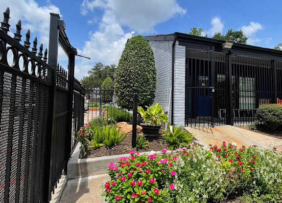 A black iron fence with a gate stands in front of a building with a black iron gate.