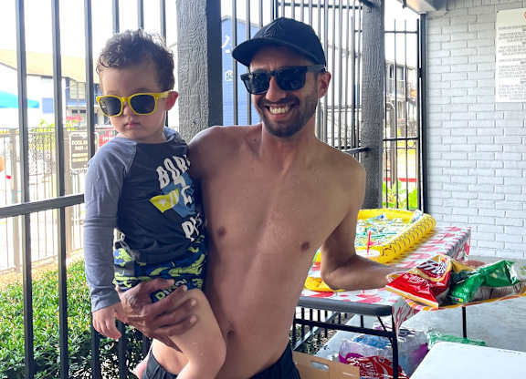 A man and a child are standing in front of a table with snacks on it.