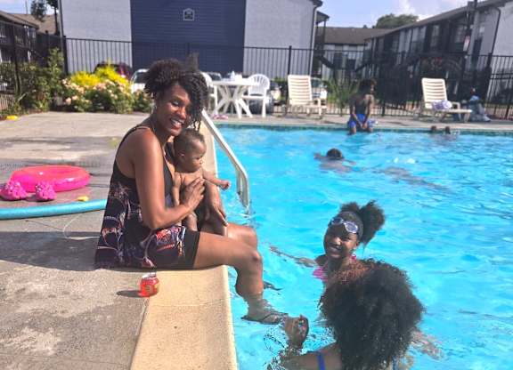 A woman holding a baby while sitting on the pool edge.