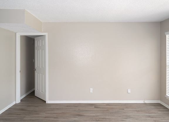 a living room with wood-like floors and a door leading to a bedroom