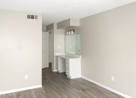 a spacious bedroom with a built-in vanity and mirror and wood-style flooring