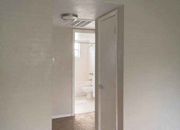 a hallway leading to a white bathroom with a toilet and sink.