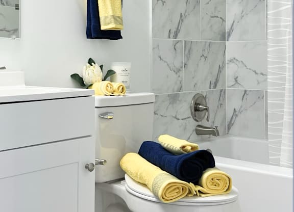 a modern bathroom with marble tile, blue and yellow towels