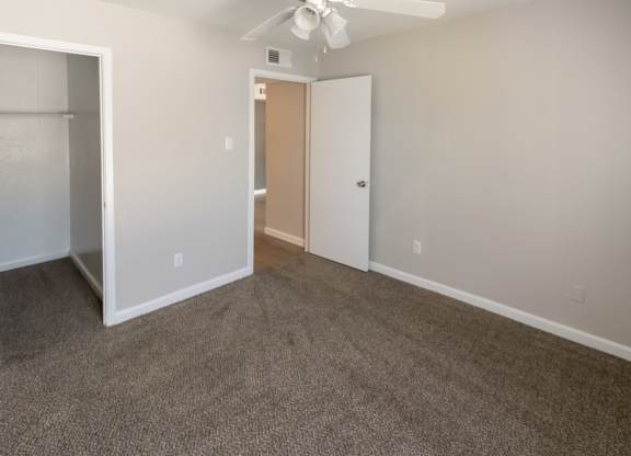 a carpeted bedroom with a ceiling fan and a large, deep closet