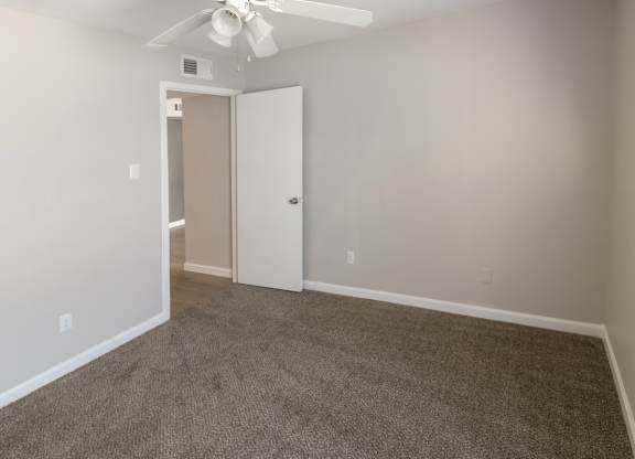 a spacious bedroom with plush carpeting and a ceiling fan with a light kit