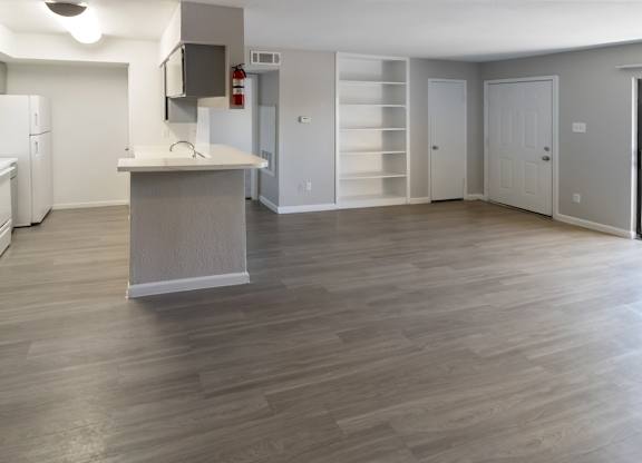 a large living room and kitchen with neutral paint and gray cabinets and white appliances and shelving